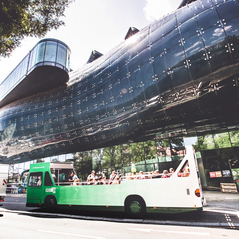 An open-top cabriolet bus stands in front of the Kunsthaus in Graz. | © Lupi Spuma