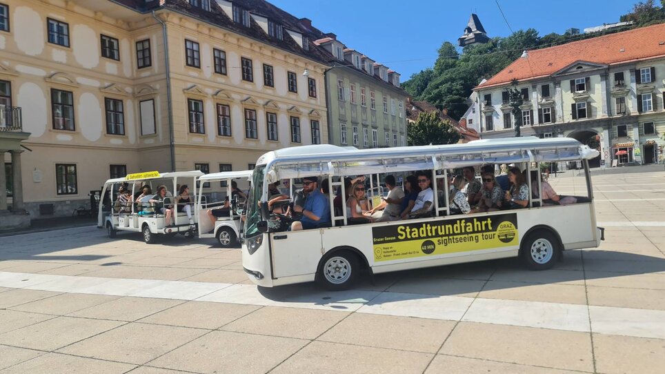 Electric shuttle on a sightseeing tour in Graz. Graz Clock Tower and historical buildings in the background. | © Graz Stadtrundfahrten