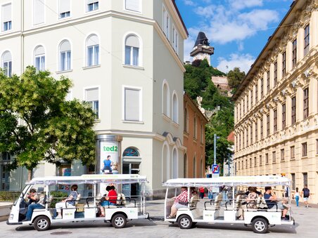 An electric shuttle on a city tour in Graz, with the Graz Clock Tower in the background. | © Graz Tourismus - Harry Schiffer