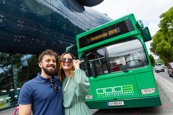 Couple poses in front of green bus in Graz, Genuss Tour 2020. | © Graz Tourismus - Werner Krug
