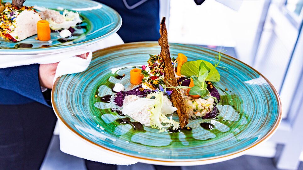 Artistically presented dish on blue plate, served by waiter. | © Graz Tourismus - Werner Krug