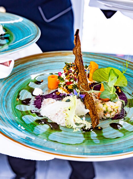 Artistically presented dish on blue plate, served by waiter. | © Graz Tourismus - Werner Krug