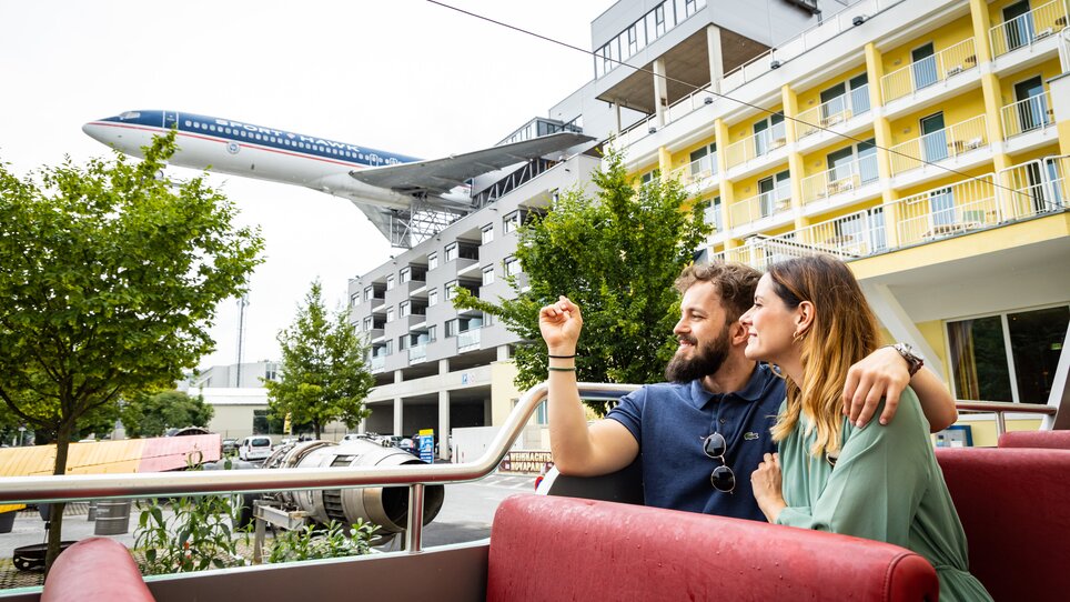 Couple enjoying the view during a culinary tour in a convertible bus - in the background an aeroplane from the NOVAPARK aeroplane restaurant. | © Graz Tourismus - Werner Krug
