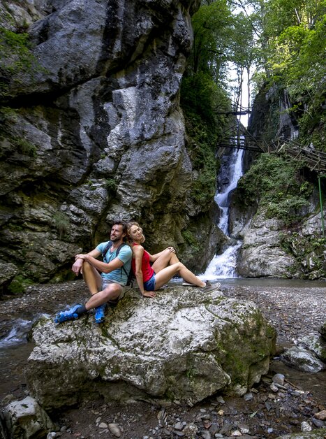 A couple sitting on a rock next to a waterfall in Kesselfallklamm. | © Region Graz - Tom Lamm