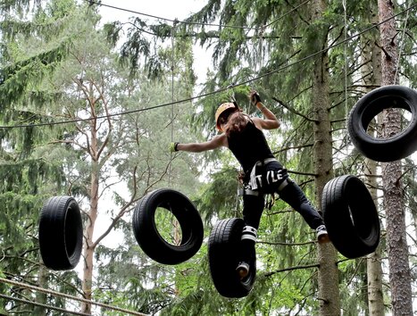 A girl balances on tires in a tree climbing course. | © Kletterpark Schöckl - Oberlaender