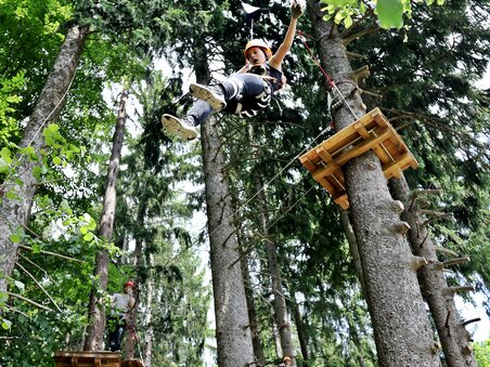 Junge schwingt an einem Seil zwischen Bäumen, während andere Kletterer in der Nähe sind. | © Kletterpark Schöckl - Oberlaender