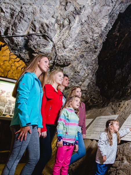 Familie erkundet die Lurgrotte Peggau mit einem Blick auf die Statue und Informationsschilder. | © TV Region Graz - Mias Photoart