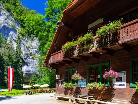 A wooden house with flowers above the entrance, surrounded by trees and rocks. | © TV Region Graz - Harry Schiffer