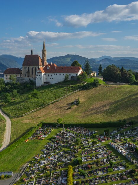 Aerial view of the Pilgrimage Church of Maria Strassengel with a cemetery in the foreground. | © TV Region Graz - PicFly