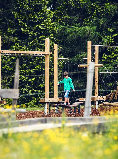 A boy plays on a climbing structure in a playground setting. | © Lupi Spuma
