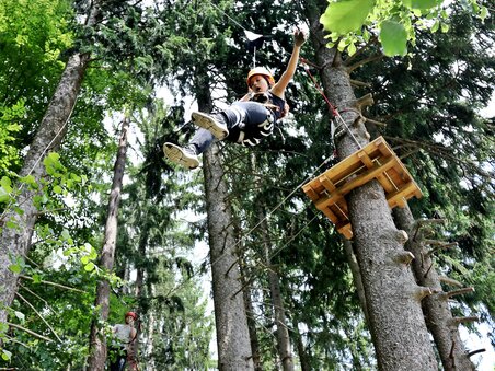 A person swings between the trees in a rope park.