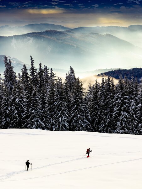 Two people hiking through freshly fallen snow in a winter landscape. | © Region Graz - Harry Schiffer
