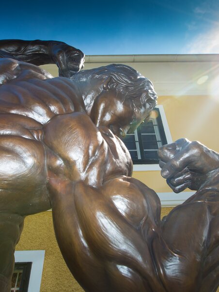Nahaufnahme einer beeindruckenden Bronzestatue des Bodybuilders Arnold Schwarzenegger mit muskulösem Oberkörper. | © Region Graz - Harry Schiffer