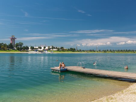 Zwei Personen entspannen auf einem Steg am Schwarzlsee bei blauem Himmel. | © Region Graz - Harry Schiffer