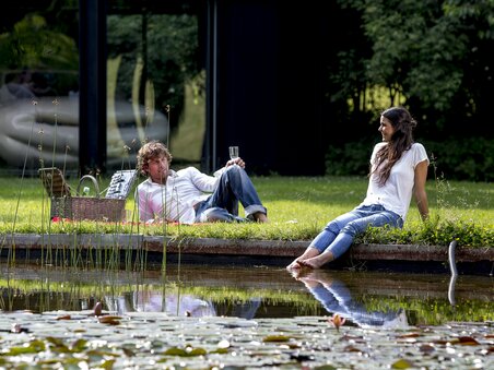 Zwei Personen entspannen am Ufer eines Gewässers im österreichischen Skulpturenpark. | © Region Graz - Tom Lamm