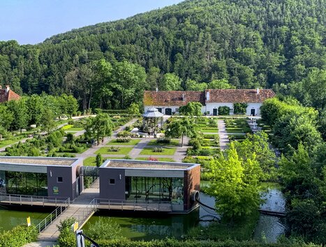 A beautiful garden of Herberstein Castle featuring modern buildings and green mountainous landscape in the background. | © Steiermark Tourismus - Klein