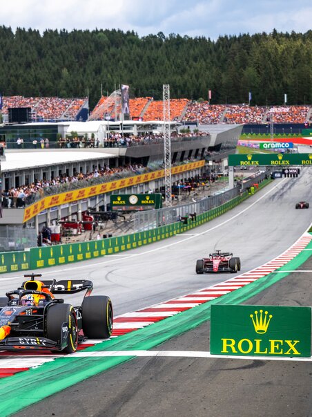 Formula 1 race cars speeding on the Red Bull Ring racing circuit, with packed grandstands full of cheering spectators. | © Joerg Mitter - Red Bull Content Pool