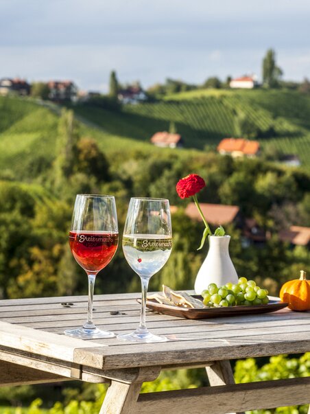 Two wine glasses on a table with a view of vineyards. | © Steiermark Tourismus - ikarus