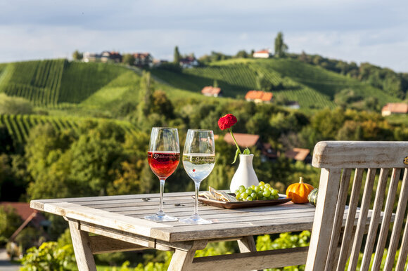 Two wine glasses on a table with a view of vineyards. | © Steiermark Tourismus - ikarus