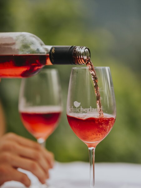 Two wine glasses being filled with rosé-colored Schilcher wine from a bottle – a regional specialty from Western Styria, Austria. | © Schilcherland Steiermark - Lupi Spuma