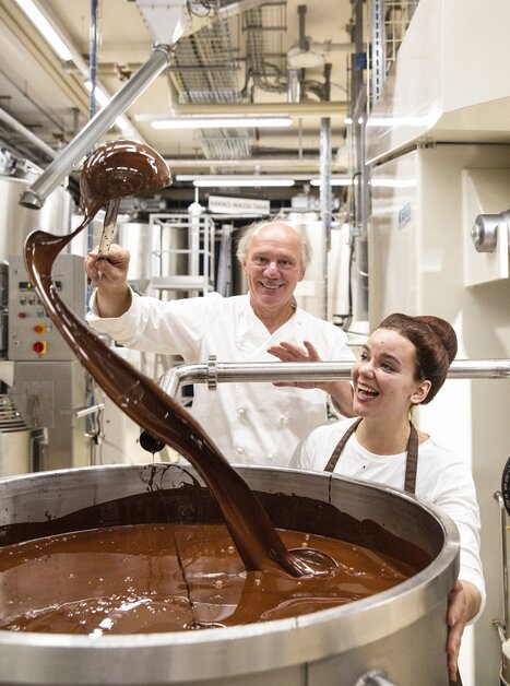 Two people working in a chocolate factory with liquid chocolate. | © Zotter Schokolade