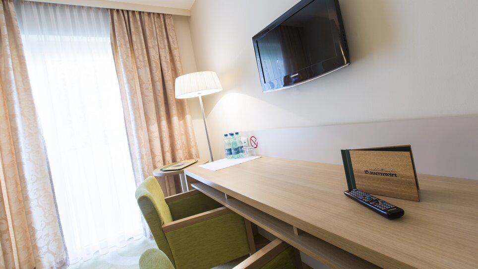 Camera d'hotel accogliente con scrivania, TV e vista sulla finestra. | © Bauernwirt