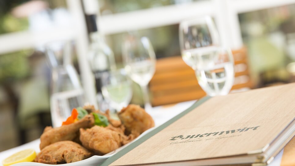 Un tavolo apparecchiato con un menù e pollo fritto. | © Bauernwirt