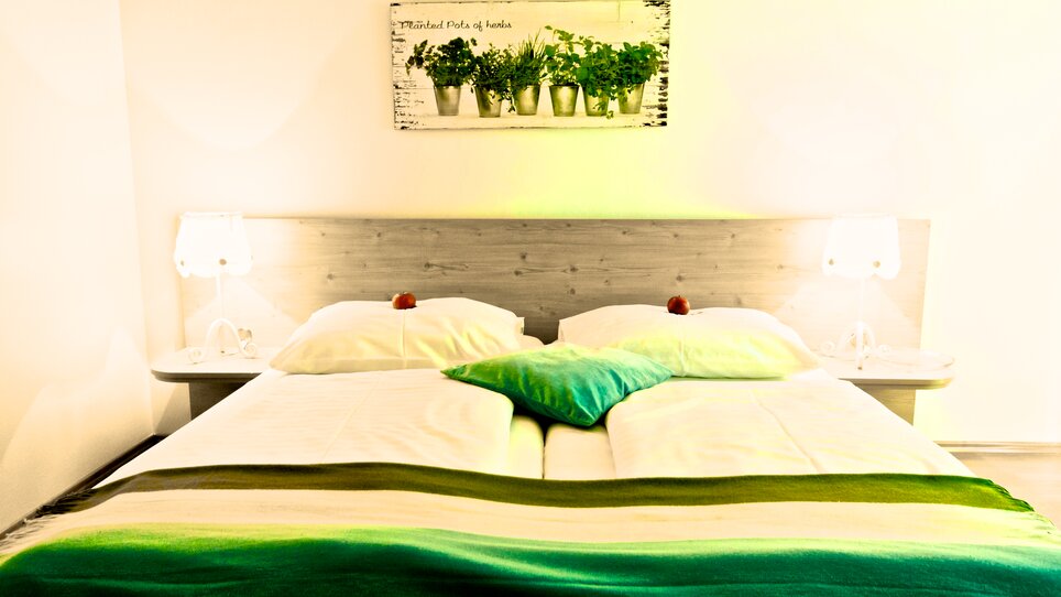 A double room with two beds, pillows, and a plant picture on the wall. | © Zur Steirerstubn