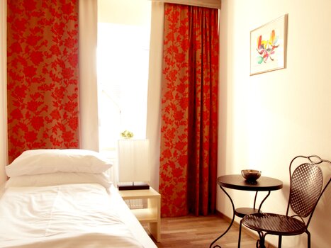 Single room with red curtains and table at Gasthof Pension Zur Steirerstub'n. | © Zur Steirerstubn