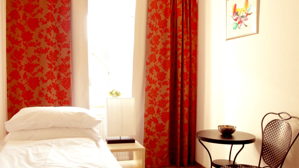 Single room with red curtains and table at Gasthof Pension Zur Steirerstub'n. | © Zur Steirerstubn