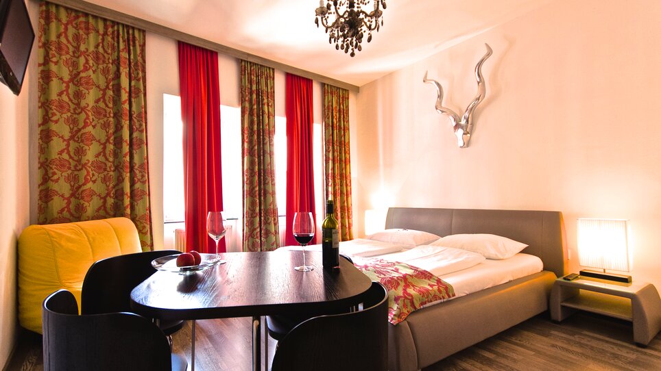 A room featuring a double bed, table, chairs, and a TV. | © Zur Steirerstubn