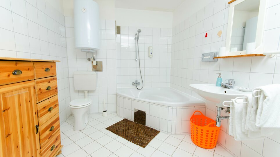 Bright bathroom featuring a bathtub, shower, and wooden cabinet. | © Zur Steirerstubn