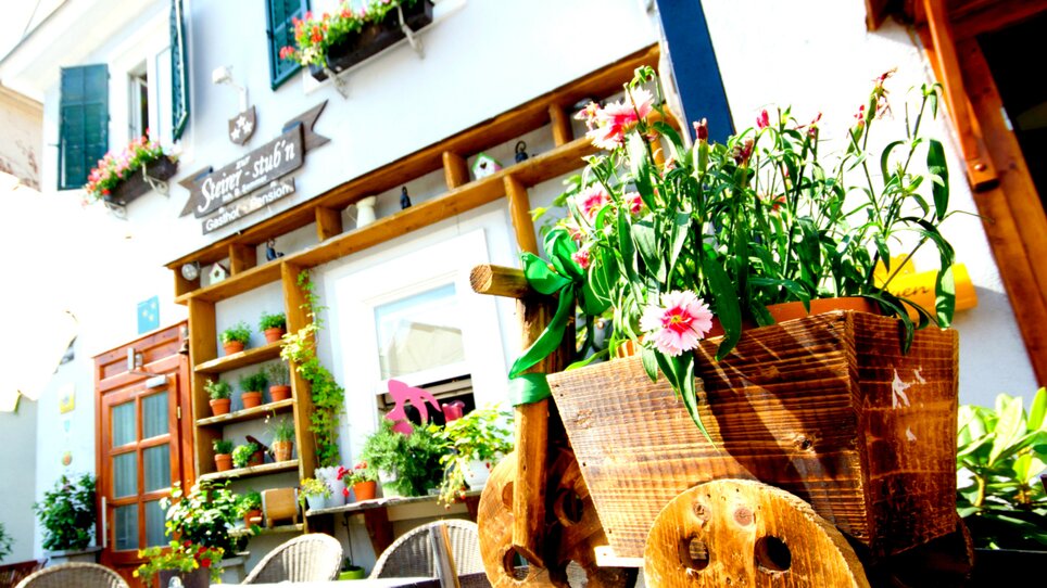 View of Guesthouse Pension Zur Steirerstub'n with wooden cart full of flowers. | © Zur Steirerstubn