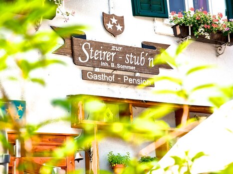 View of the Gasthof Pension Zur Steirerstub'n with a wooden sign. | © Zur Steirerstubn