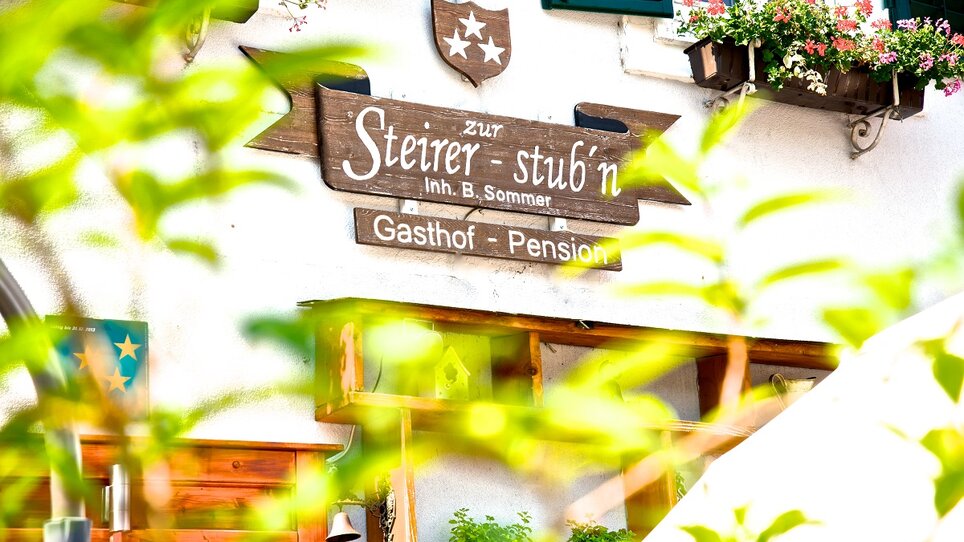 View of the Gasthof Pension Zur Steirerstub'n with a wooden sign. | © Zur Steirerstubn