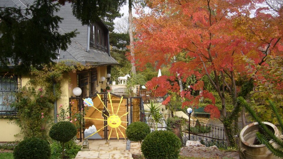 View of the entrance with a colorful fence and red trees. | © Legenstein