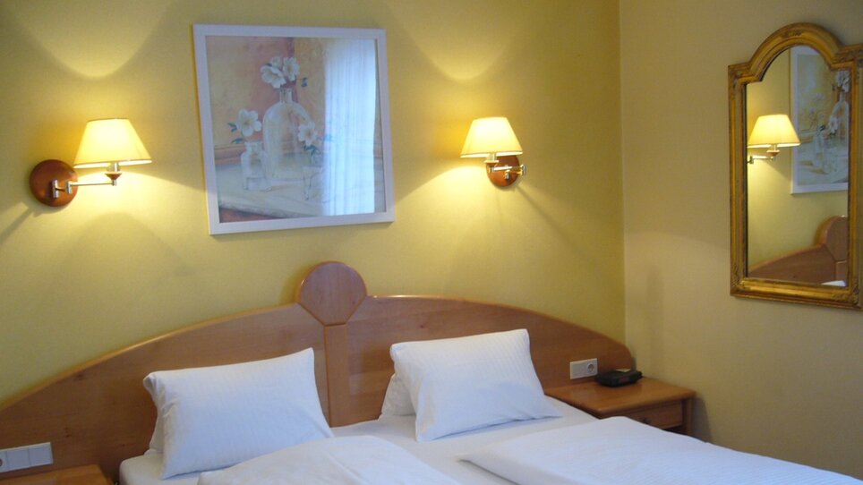 Bedroom with two beds, nightstands, and wall mirror. | © Legenstein