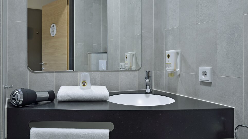 Badezimmer mit Waschbecken, Handtuch und Fön. | © B&B Hotel Graz City Süd
