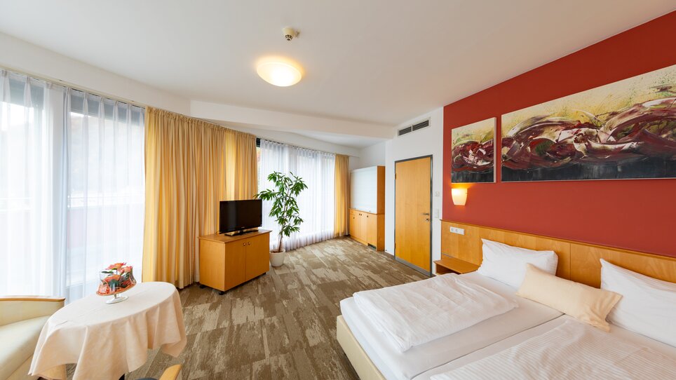 Bright hotel room with two beds, TV, and a table. | © Harry Schiffer
