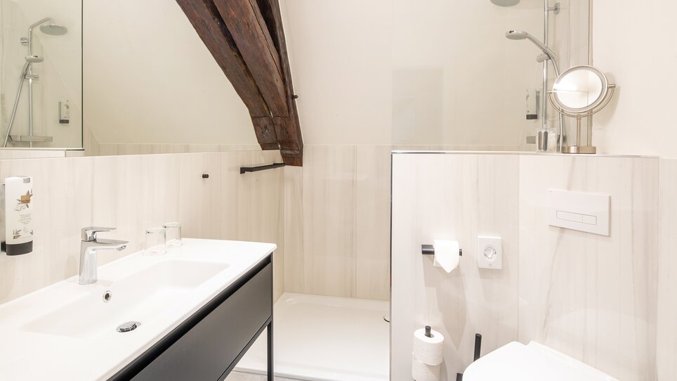 Bathroom with shower, sink, and toilet, featuring wooden ceiling beams. | © Robert Illemann