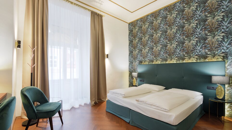A stylish bedroom featuring light colors and plant patterns on the wall. | © Hotelpartner