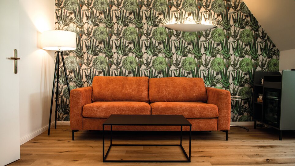 An orange couch in front of a green wallpaper with a table. | © Robert Illemann