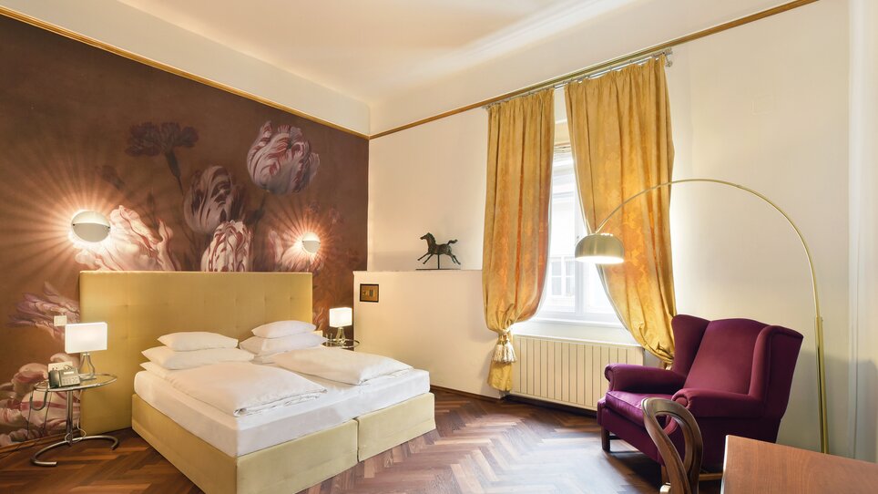 An elegant hotel room with a classic bed and beautiful wall painting. | © Robert Illemann