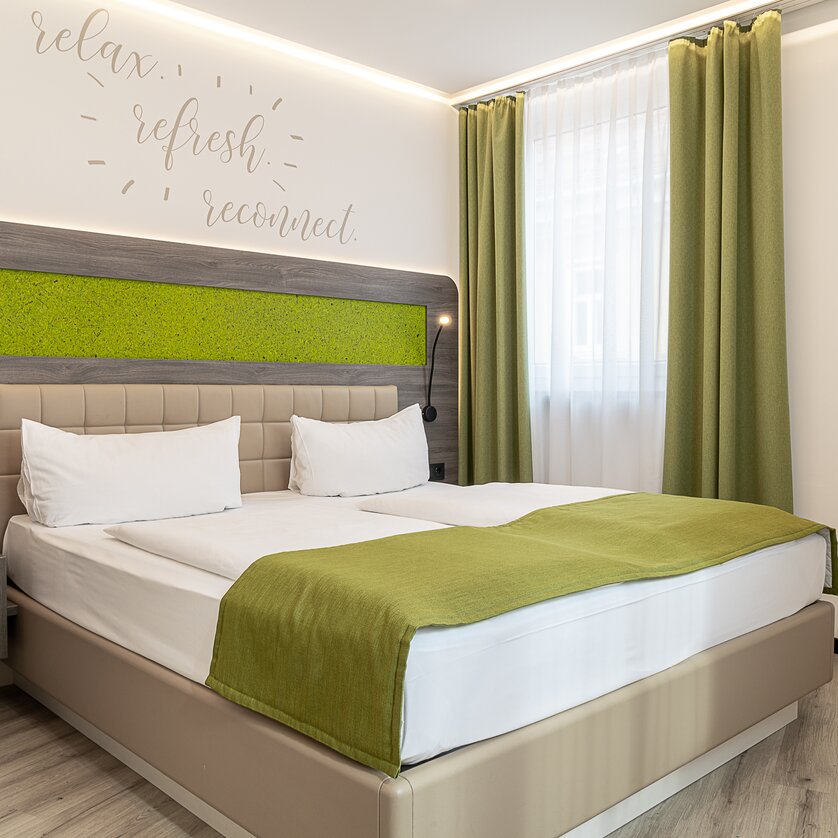 Una camera da letto con un letto matrimoniale, copripiumino verde e frasi ispiratrici sul muro. | © Chrizz Rooms