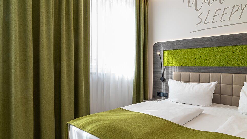 Una stanza con un letto, tende verdi e decorazione murale. | © Chrizz Rooms