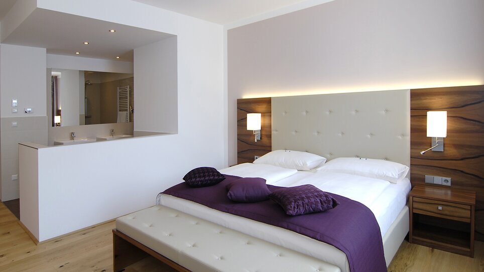 Ein modernes Schlafzimmer mit einem Doppelbett und einem Badezimmer im Hintergrund. | © Hotel Feichtinger