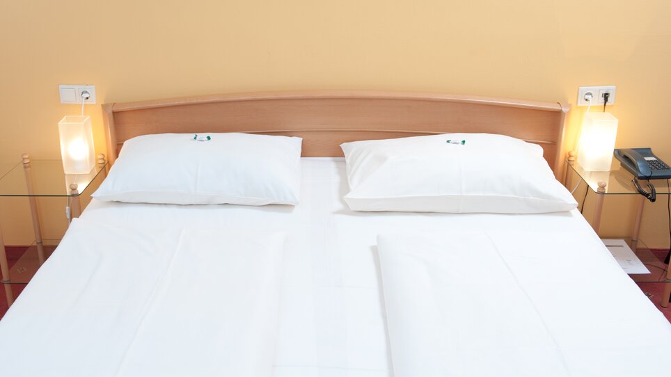 Ein Doppelbett mit zwei weißen Kissen und Nachttischen. | © Feichtinger