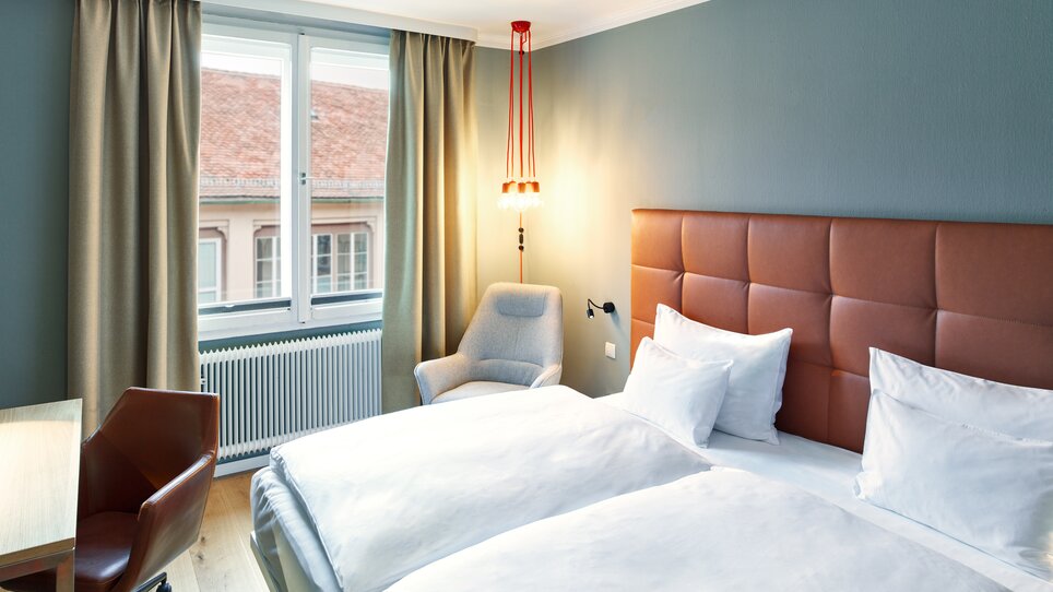 Helles Hotelzimmer mit zwei Betten und einem Sitzbereich.