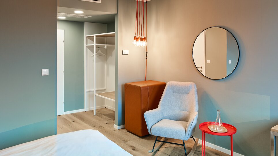 Ein gemütliches Zimmer mit hellen Wänden, einem Stuhl und einem Spiegel.