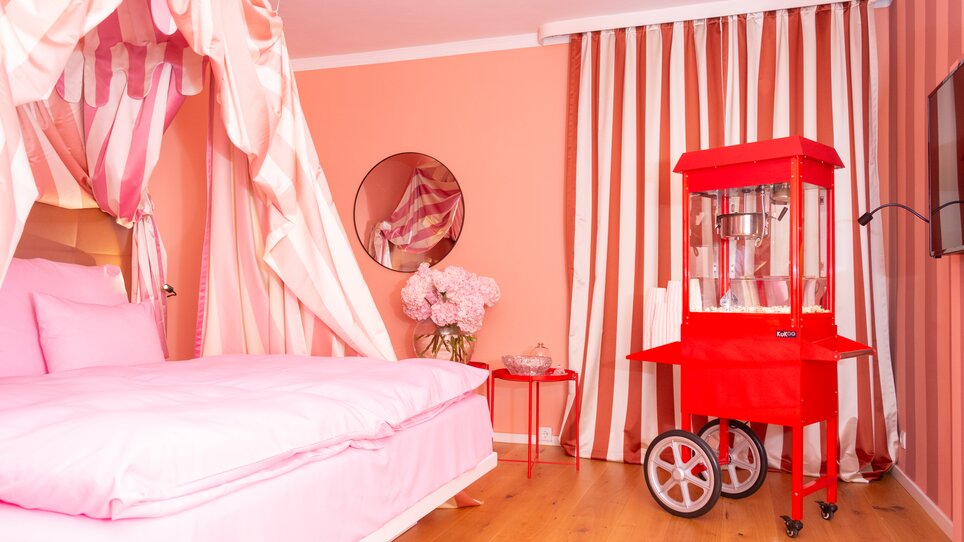 Ein verspieltes Schlafzimmer mit rosa Bett, gestreiften Vorhängen und einer roten Popcornmaschine.